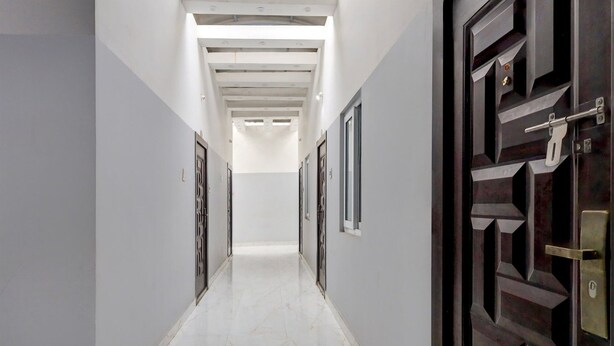 Un pasillo con suelo de mármol blanco, techo con iluminación empotrada y puerta con diseño geométrico.