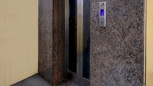 Un ascensor con una pantalla digital que muestra el número 3, ubicado en un pasillo con paredes de granito.