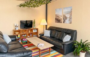 Una sala de estar con un sofá de cuero negro, una mesa de centro de madera, un televisor, una lámpara, una estantería y una planta.