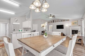Amplia sala de estar con una mesa de comedor de madera, sillas blancas, chimenea y ventilador de techo.