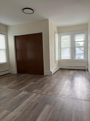 Une pièce dotée d’un parquet, d’une grande porte en bois foncé et d’une fenêtre avec des stores.