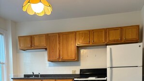 Eine Küche mit Holzausstattung, einem weißen Kühlschrank, einem Herd und einer Leuchte.