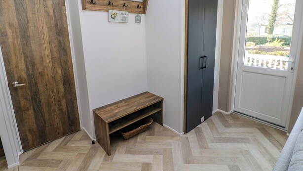 Una stanza con una porta in legno, una panca, un appendiabiti con ganci e un armadio grigio, e una finestra che si affaccia sul verde.