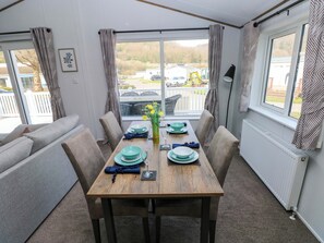 A dining area with a table set for four, a sofa, and a view of a parking area through large windows. - 148 Dukes Meadow (Carmarthen)