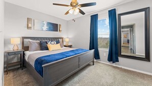 Een slaapkamer met een bed, twee nachtkastjes, een plafondventilator, een groot raam met gordijnen en een spiegel.