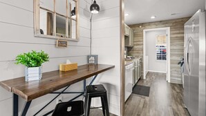Een keuken met een houten aanrecht, een hangende lamp, een koelkast en een deur naar een andere kamer.
