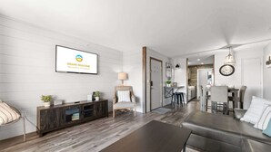 Een moderne woonkamer met een bank, salontafel en televisie. Er is een eethoek met stoelen en een keuken op de achtergrond.