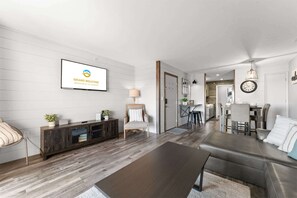 A modern living room with a sofa, coffee table, and TV. There's a dining area with chairs and a kitchen in the background. - Branson Heights Retreat (Branson)