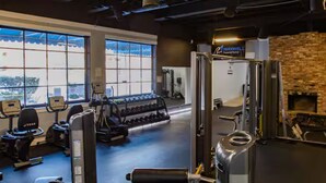 A gym with exercise equipment, a brick wall, and large windows.