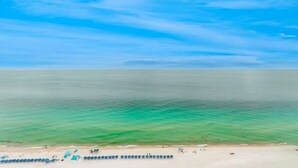 Ein Strand mit klarem türkisblauem Wasser, einer Reihe blauer Sonnenschirme und einem sandigen Ufer.