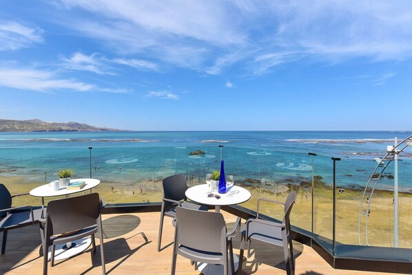 Una zona salotto all'aperto con vista libera sul mare, tavoli e sedie e una ringhiera in vetro.