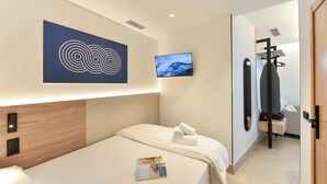 Ett hotellrum med en säng, en väggmonterad TV, en handduk på sängen, en träpanel som huvudgavel och en dörr som leder till ett badrum.