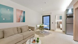 A modern living room with a sofa, a dining table with chairs, a kitchen area with a refrigerator, and a door leading to another room. - 1 bedroom interior apartment (Las Palmas de Gran Canaria)