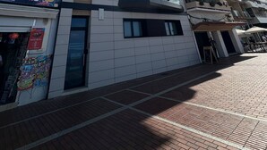 En bygning med flere etager, facade med fliser, et synligt butiksvindue med et skilt, og en klar himmel med solskin.