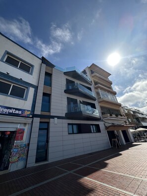 A multi-story building with a tiled facade, a visible storefront with a sign, and a clear sky with the sun shining. - Double with balcony and sea view (Las Palmas de Gran Canaria)