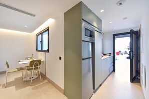 A modern kitchen with a built-in oven and microwave, a dining area with a table and chairs, and a view of the outside through a door. - 1 bedroom penthouse apartment (Las Palmas de Gran Canaria)