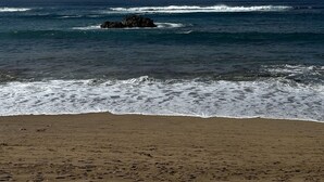 Une plage avec des vagues, un promontoire rocheux et un ciel dégagé.