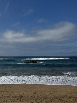 Ein Strand mit Wellen, einem Felsen und blauem Himmel.