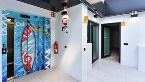 Un couloir d’hôtel moderne avec un décor mural bleu et blanc, du matériel de sécurité incendie et des portes numérotées.