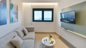 A modern living room with a sofa, a round coffee table with drinks and snacks, a TV, and a window with a view of the sea. - Sea view family studio first floor (Las Palmas de Gran Canaria)