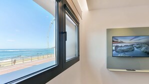 A room with a large window overlooking a beach, a television mounted on the wall, and a tiled floor. - Sea view family studio first floor (Las Palmas de Gran Canaria)