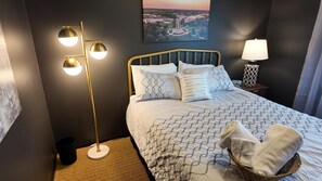 Une chambre d’hôtel bien rangée, avec un lit, un lampadaire, une table de chevet avec une lampe, une horloge et un tableau encadré au mur.