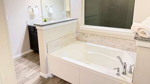 Ein Badezimmer mit einer weißen Badewanne, einem großen Spiegel und einem Fenster.