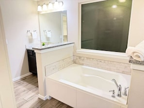 A bathroom with a white bathtub, a large mirror, and a window. - Villa Horizonte Deluxe (Midland)