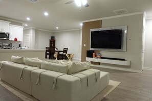 A modern living room with a sofa, a flat-screen TV mounted on the wall, a dining area with chairs and a table, and a kitchen with appliances. - Villa Horizonte Deluxe (Midland)