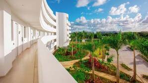 Een modern hotel met een gebogen gevel, een centrale witte toren en een aangelegde tuin met palmboom.