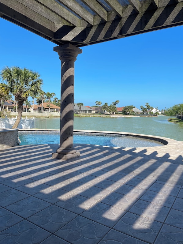 A pool area with a stone column, tiled flooring, and a clear view of a residential area in the background.