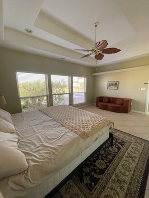 A bedroom with a bed, a ceiling fan, a window, a sofa, and a rug.