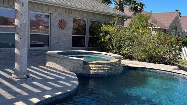 Piscina com borda de pedra, pérgula e vista para uma área residencial.