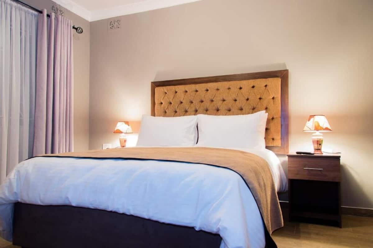 Quarto de hotel com uma cama grande, duas mesas de cabeceira com luminárias, uma cabeceira e uma cortina.