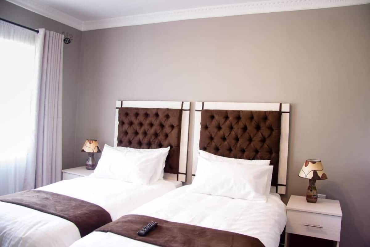 Quarto de hotel com duas camas, uma janela com cortinas e abajures.