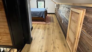 A narrow attic bedroom with a bed, wooden walls, and a sloped ceiling.
