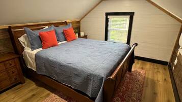 A bedroom with a wooden bed, a nightstand, a window with blinds, and a wooden floor.