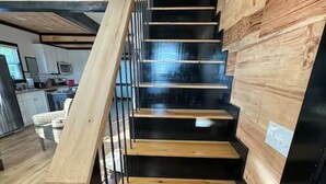 A staircase with wooden steps and black railings, leading to a room with a kitchen and a dining area.