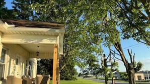 A covered porch with outdoor seating, a lawn, and a tree.