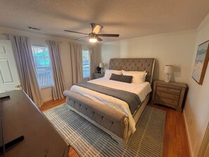 A bedroom with a bed, a ceiling fan, a nightstand, a lamp, and a window with curtains. - THE RIVERSIDE RETREAT - 30 minutes from SAVANNAH GA- FLOAT/BOAT/RINSE/REPEAT (Midway)