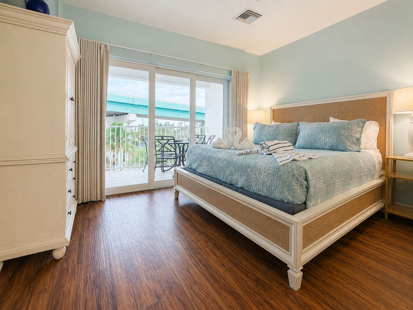 A bedroom with a bed, a wardrobe, a balcony with a view, and a table with chairs.