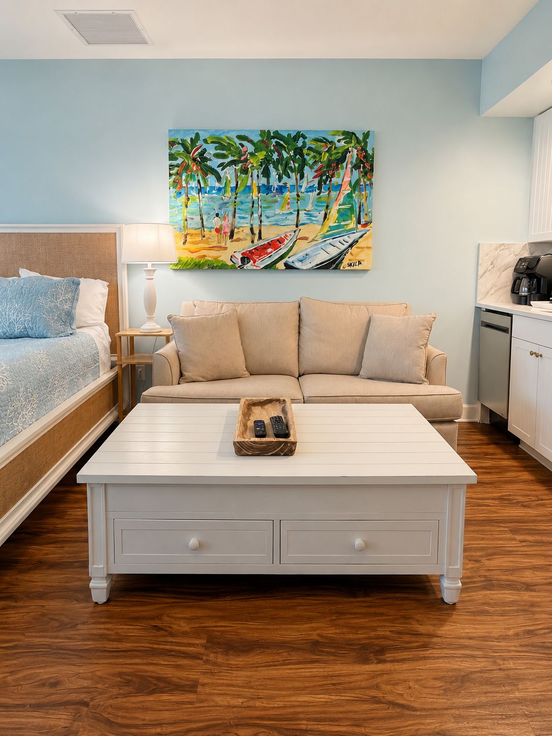 A hotel room with a bed, a sofa, a coffee table, and a painting of a beach scene.