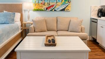 A hotel room with a bed, a sofa, a coffee table, and a painting of a beach scene.