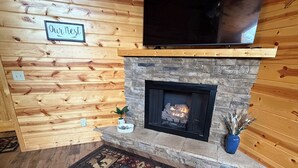 A log cabin interior with a stone fireplace, a mounted television, and a patterned rug. - 
Charming 2 bed room mountain hideaway in Murphy (Murphy)