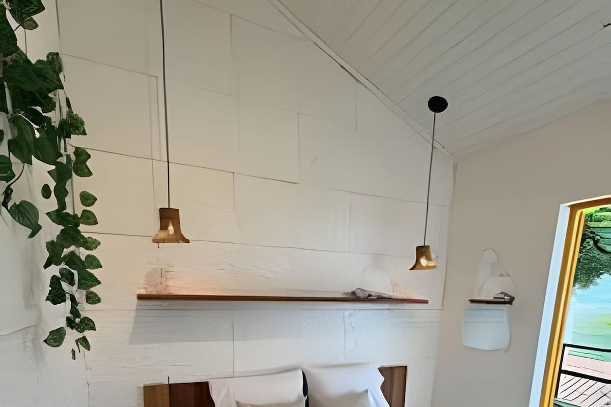 Ein Schlafzimmer mit Bett, Nachttischlampen, einer hängenden Pflanze, einem Fenster mit Blick und einem Holzregal über dem Bett.