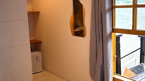 Ein kleiner Raum mit einem weißen Kühlschrank, einem Holzregal, einem Spiegel und einem Fenster mit Vorhängen.