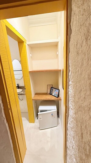 Una habitación compacta con una banca integrada, un refrigerador pequeño y un cuadro enmarcado sobre la banca.