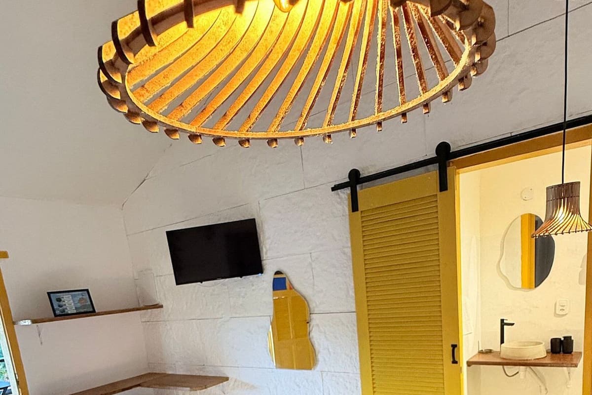 Ein Schlafzimmer mit Bett, Fernseher, gelber Tür und einer Pendelleuchte.