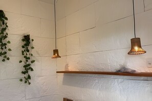 Una habitación con paredes blancas con textura, un estante de madera y lámparas colgantes.