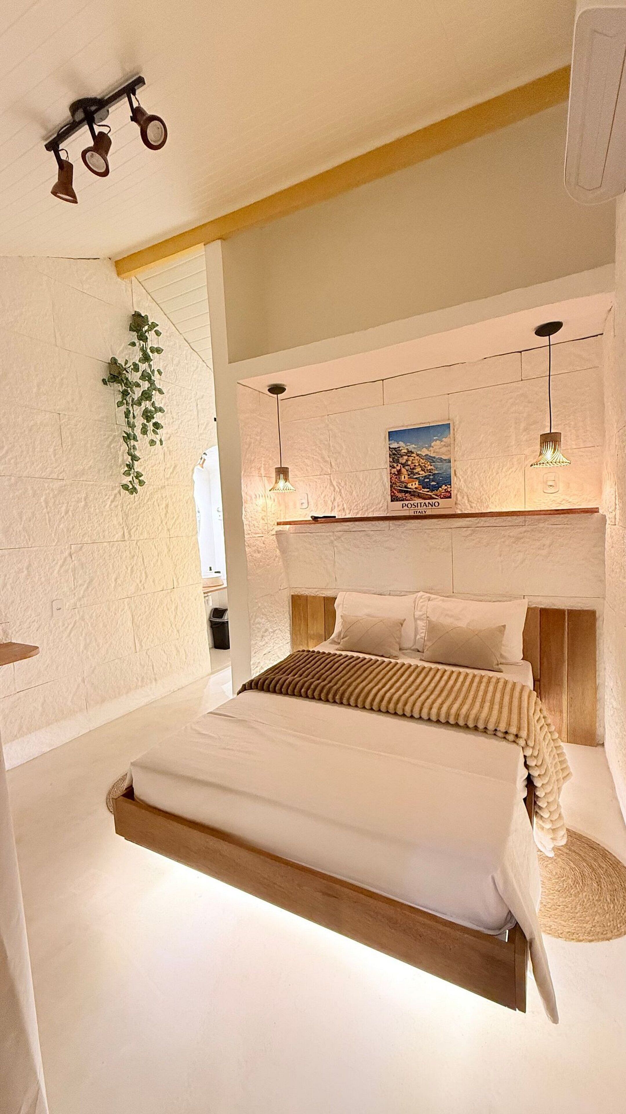 A bedroom with a bunk bed, a hanging plant, a painting of Positano, Italy, and a ceiling light fixture.
